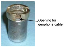 Photograph shows a ground ring that has been mounted on a geophone. An arrow indicates the location of the opening for geophone cable.