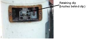 Photograph shows brushes and retainer. An arrow indicates the location of the retaining clip open parenthesis brushes are located behind clip close parenthesis.