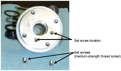 Photograph shows the top view of a catch flange and two set screws. Arrows indicate the locations of the two set screws open parenthesis use medium-strength thread locker when installing close parenthesis.