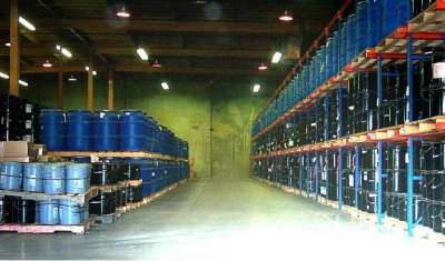 Figure 1. Photograph. Photograph of the MRL storage facility. This picture shows an aisle in a large facility that looks like a warehouse. On the left side of the aisle are two shelves with large blue barrels stacked on them. The ride side of the aisle has three shelves stacked blue and black barrels. 