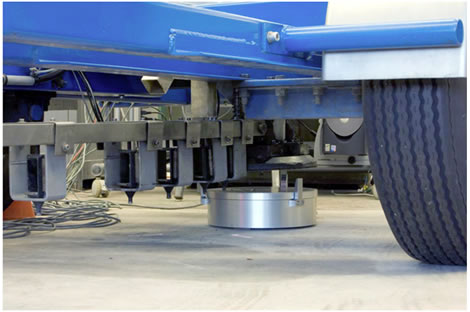 Figure 106. Photo. Reference load cell positioned under the FWD load plate. This photo is a view of the underside of the Dynatest ® falling weight deflectometer (FWD) with the reference load cell aligned under the FWD load plate. The reference load cell is seen underneath the load plate, and the wheels from the FWD trailer can be seen.