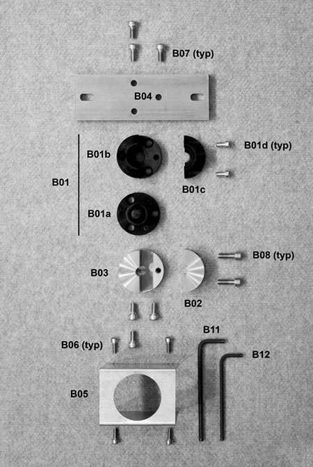 Figure 111. Photo. Parts and tools for ball-joint assembly. This figure shows the parts and tools necessary for ball-joint assembly. The parts are spread out on a flat surface, and the picture is taken above them. The parts and tools include a ball-joint, ball, socket, clamps, screws, a clamp base, a base bar, a rest stop, and two wrenches.