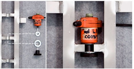 Figure 119. Photo. Placement of the accelerometer box on the geophone stand. This photo shows the vertical geophone stand on a flat surface with two handles coming out of each side. The accelerometer box is shown in position on the accelerometer shelf below the handles. The two attachment screws are shown to the side.