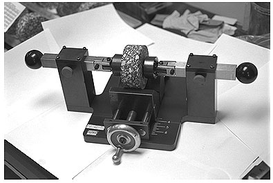 Figure 9 provides a picture of a typical gauge point mounting device.  This system is used to precisely mount the gauge points on the sample prior to testing.  A typical asphalt core specimen is resting in the mounting device ready for the gauge points to be mounted