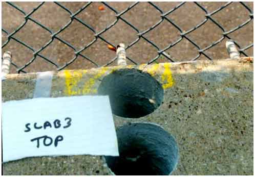 Figure 13. Photo. Delamination (marked in yellow) found on the top surface of slab 3. This photograph shows a delamination marked in yellow on the top surface of slab 3 and corrosion of the rebar just inside the concrete that also resulted in a delamination.