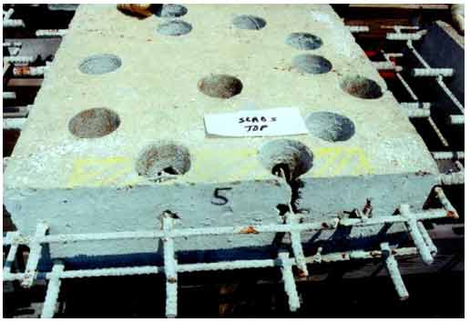 Figure 17. Photo. Delaminations (marked in yellow) and concrete failure near a core hole on slab 5. This photograph shows delaminations marked in yellow along the edge of slab 5 and adjacent to a core hole with vertical cracks. Rust stains in some core holes adjacent to the ends of rebars are also visible in the photo.
