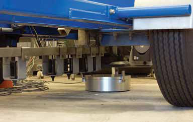 Calibrating equipment is shown beneath an falling-weight deflectometer between the tires. A silver colored round cylinder is part of the equipment.