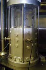 . The photograph shows a metal and glass testing cylinder with metal rods partly visible inside and wires attached outside.
