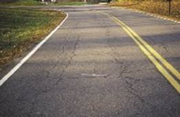 Photo. Distressed asphalt pavement on a two-lane road.