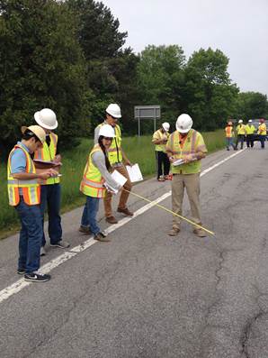 Photo. Workers in safety vests and helmets examining pavement from the side of a highway.