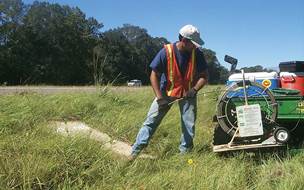 Figure 6.15. Photo. Worker in safety vest and helmet operating equipment at concrete drainage near a highway.