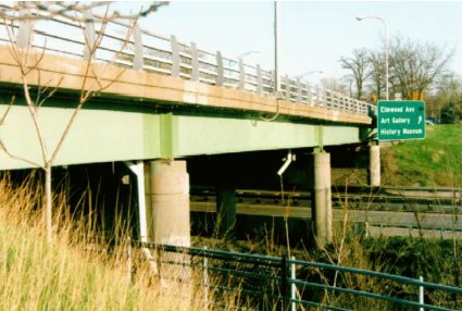 General view of the Elmwood Avenue bridge over NY Route 198, Buffalo, NY. This photo shows the Elmwood Avenue bridge from a side vantage point. Three supporting circular columns are visible. A railing several feet high runs along the one edge of the bridge deck. The surface of the bridge deck is not visible.