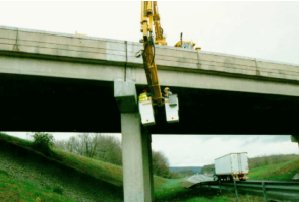 Photo D shows a vehicle parked on the bridge deck with a long mechanical arm bent to extend underneath the bridge deck. An inspector is in one of the two compartments at the end of the arm. 