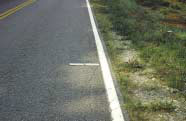 FIGURE 12.  Distress Type ACP 3 - Low Severity Edge Cracking, Color photograph of asphalt concrete pavement with distress type ACP 3 - low severity edge cracking.  The width of the cracking is approximately 400 m as indicated by the 500-mm scale pictured in the center of the photograph, starting at the unpaved shoulder and ending beyond the edge stripe, and extending along the entire length of the lane.