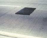 FIGURE 120.  Distress Type CRCP 11 - Low Severity Asphalt Concrete Patch, Color photograph of continuously reinforced concrete pavement with distress type CRCP 11 - low severity asphalt concrete patch.  The rectangular patch extends from the center line joint through the inner wheel path.  No faulting, settlement, or pumping is evident.