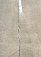 FIGURE 129.  Distress Type CRCP 13 - Low Severity Spalling of a Longitudinal Joint, Color photograph of continuously reinforced concrete pavement with distress type CRCP 13 - low severity spalling of a longitudinal joint.  The spalled areas at the pavement joint, with widths up to approximately 25 mm, extend along approximately 50% of its length with loss of some material.