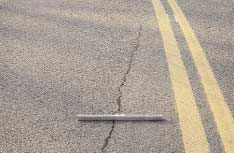 FIGURE 15.  Distress Type ACP 4b - High Severity Longitudinal Cracking Not in the Wheel Path, Color photograph of asphalt concrete pavement with distress type ACP 4b - high severity longitudinal cracking not in the wheel path.  As indicated by the 500-mm scale pictured in the center of the photograph, the crack is approximately 25 mm wide, and extends from the inner wheel path toward the center line along the entire length of the lane.