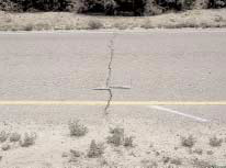 FIGURE 21.  Distress Type ACP 6 - High Severity Transverse Cracking, Color photograph of asphalt concrete pavement with distress type ACP 6 - high severity transverse cracking.  The deep, uneven crack extends across the entire road from the unpaved shoulder to the opposite unpaved shoulder.  As indicated by the 500-mm scale pictured in the center of the photograph, the crack width varies between approximately 25 mm and 50 mm.