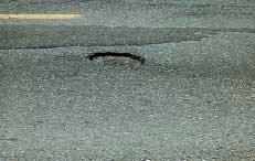 FIGURE 28.  Distress Type ACP 8 - Moderate Severity Pothole, Color photograph of asphalt concrete pavement with distress type ACP 8 - moderate severity pothole.  The area of deterioration near the center line is a bowl-shaped hole in the pavement surface with cracking around its edges.