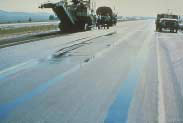 FIGURE 33.  Distress Type ACP 9 - Standing Water in Ruts, Color photograph of asphalt concrete pavement with distress type ACP 9 - standing water in ruts.  The photo shows one lane of a two-lane road where water has collected in ruts in the wheel paths along the entire length of the road visible in the photograph.