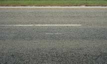 FIGURE 36.  Distress Type ACP 11 - Discoloration, Color photograph of asphalt concrete pavement with distress type ACP 11 - discoloration.  The discolored surface of the wheel paths along the length of the lane indicates low level bleeding of excess bituminous binder.  A 500-mm scale is pictured in the center of the photograph, and indicates that the lane is approximately 2500 mm long.