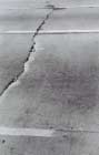 FIGURE 78.  Distress Type JCP 12 - Faulting of Transverse Cracks, Color photograph of jointed portland cement concrete pavement with distress type JCP 12 - faulting of transverse cracks.  The picture shows a transverse crack with associated spalling and corner breaks that extend across two lanes of the pavement.