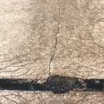 FIGURE 91.  Distress Type CRCP 1 - Moderate Severity D Cracking at Transverse Crack
Color photograph of continuously reinforced concrete pavement with distress type CRCP 1 - moderate severity D Cracking at transverse crack.  There are multiple closely-spaced, crescent-shaped hairline cracks surrounding all sides of the transverse crack where it meets the pavement joint.