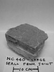  Figure 3-47 (c):  Photographs.  Cores and specimens evaluated from NC-440-015. This figure is comprised of three photographs labeled A, B, and C.  Photograph A shows core NC440001A.  The core was taken at the transverse joint from the road surface down to a depth of 26.5 centimeters.  Some cracking is seen approximately half way down the core.  Photograph B is core NC440001E.  This core was taken away from the joint from the road surface down to a depth of 26.5 centimeters.  Photograph C is a specimen from NC440, is 10 centimeters across.  It is a piece of spall that has come up from a joint.  