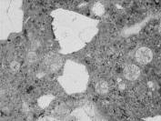  Figure 3-50 (a):  Photographs.  Petrographic micrographs from spall obtained from NC-440-015 showing ettringite filled entrained air voids.  Ettringite growths are unusually dense.  This figure is comprised of three micrographs labeled A, B, and C.  Photograph A uses a transmitted plane polarized light.  The air voids appears as light gray circles on this micrograph.  Photograph B was taken is in epifluorescent mode.  The filled air voids are more evident in this micrograph and at least seven are visible.  Photograph C uses a transmitted cross polarized light and the air voids are not easily seen.