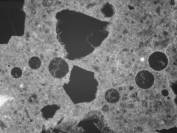   Figure 3-50 (b):  Photographs.  Petrographic micrographs from spall obtained from NC-440-015 showing ettringite filled entrained air voids.  Ettringite growths are unusually dense.  This figure is comprised of three micrographs labeled A, B, and C.  Photograph A uses a transmitted plane polarized light.  The air voids appears as light gray circles on this micrograph.  Photograph B was taken is in epifluorescent mode.  The filled air voids are more evident in this micrograph and at least seven are visible.  Photograph C uses a transmitted cross polarized light and the air voids are not easily seen.