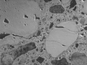  Figure 3-6 (a):  Photographs.  Stereo optical micrographs of typical cracking pattern associated with porous siltstone aggregate SD-090-019.  This figure is comprised of two photographs labeled A and B.  Photograph A is a micrograph of the siltstone aggregate. Cracking is seen running through and around the aggregate particles.  Multiple open air voids also are visible in the micrograph.  Photograph B is a micrograph of the siltstone and rhyolite aggregate.  Cracking is seen running through the aggregate and into the paste.  The aggregate rims are also visible on several of the larger particles as are several open air voids.