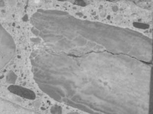 Figure 3-7 (a):  Photographs.  Stereo optical micrograph showing gel deposits in SD-090-019 aggregates.  This figure is comprised of two photographs labeled A and B.  Photograph A is a micrograph of the metamorphic aggregate.  The micrograph is centered on one large piece of aggregate that has a large crack running through it.  Photograph B is a micrograph of the siltstone aggregate.  Cracking can be seen running through the aggregate.  Several areas in the paste appear bright white in color, which is caused by reaction products in the paste.