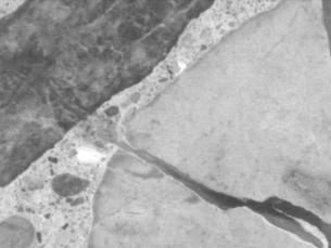 Figure 3-7 (b):  Photographs.  Stereo optical micrograph showing gel deposits in SD-090-019 aggregates.  This figure is comprised of two photographs labeled A and B.  Photograph A is a micrograph of the metamorphic aggregate.  The micrograph is centered on one large piece of aggregate that has a large crack running through it.  Photograph B is a micrograph of the siltstone aggregate.  Cracking can be seen running through the aggregate.  Several areas in the paste appear bright white in color, which is caused by reaction products in the paste.