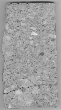  Figure 3-83:  Photograph.  Polished slab from core IA-002-002-001A.  The image is a photograph of a slab from the project site.  The slab has an irregular surface along the left-hand side of the core, which provides a cross-sectional view of the transverse joint texture.  The slab is cracked approximately one-third of the way from the bottom.