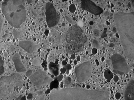  Figure 3-84:  Photograph.  Stereo micrograph showing air void structure of IA-002-002-001A. Image is magnified 7.5 times.  This image is a stereo micrograph and shows the many small, unfilled air voids within the specimen.  The air voids appear as dark holes within the specimen.