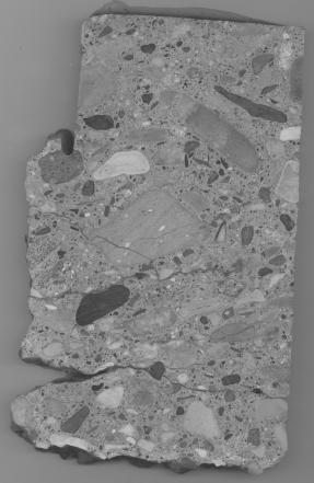  Figure 3-8 (a):  Photographs.  Slab 1B stained with sodium cobaltinitrite/rhodamine B from SD-090-019-001.  This figure is comprised of three photographs of slab 1B labeled A, B, and C.  The slab was stained with sodium cobaltinitrite/rhodamine B.  Photograph A is a picture of stained slab 1B, which is cracked at the bottom.  Photograph B is a stereo optical micrograph of a reactive porous siltstone particle from slab 1B. Internal cracking can be seen in the aggregate particle.  Photograph C is a stereo optical micrograph of a reactive volcanic particle.  Internal cracking can also be seen in this picture running through the aggregate particle.  Several areas in and around the aggregate particle appear white in color, which could be caused by reaction products, although this is not certain