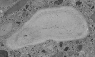  Figure 3-8 (b):  Photographs.  Slab 1B stained with sodium cobaltinitrite/rhodamine B from SD-090-019-001.  This figure is comprised of three photographs of slab 1B labeled A, B, and C.  The slab was stained with sodium cobaltinitrite/rhodamine B.  Photograph A is a picture of stained slab 1B, which is cracked at the bottom.  Photograph B is a stereo optical micrograph of a reactive porous siltstone particle from slab 1B. Internal cracking can be seen in the aggregate particle.  Photograph C is a stereo optical micrograph of a reactive volcanic particle.  Internal cracking can also be seen in this picture running through the aggregate particle.  Several areas in and around the aggregate particle appear white in color, which could be caused by reaction products, although this is not certain