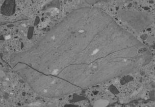  Figure 3-8 (c):  Photographs.  Slab 1B stained with sodium cobaltinitrite/rhodamine B from SD-090-019-001.  This figure is comprised of three photographs of slab 1B labeled A, B, and C.  The slab was stained with sodium cobaltinitrite/rhodamine B.  Photograph A is a picture of stained slab 1B, which is cracked at the bottom.  Photograph B is a stereo optical micrograph of a reactive porous siltstone particle from slab 1B. Internal cracking can be seen in the aggregate particle.  Photograph C is a stereo optical micrograph of a reactive volcanic particle.  Internal cracking can also be seen in this picture running through the aggregate particle.  Several areas in and around the aggregate particle appear white in color, which could be caused by reaction products, although this is not certain