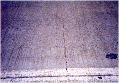 The figure consists of a photograph of a P C C pavement with a transverse crack that intersects a longitudinal crack.