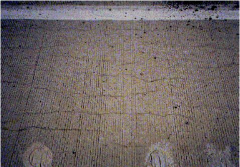 The figure consists of a photograph of a concrete pavement showing longitudinal cracking.