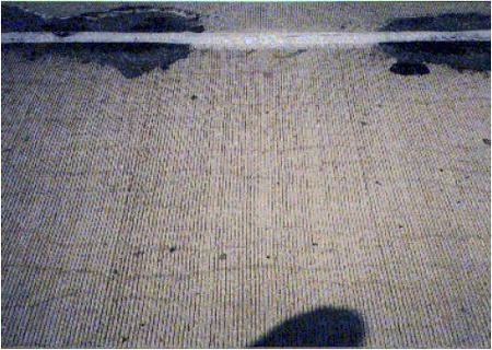 The figure consists of a photograph of a concrete pavement showing examples of asphalt patching along a joint.