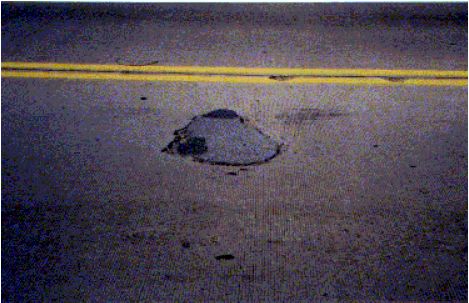 The figure consists of a photograph of asphalt patching on a concrete pavement in the center of a section in the travel lane.