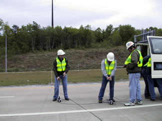 Figure 23. Photo. Impact Echo Testing- Lackawanna Valley Industrial Highway Experimental Pavement. The photo shows two workers monitoring devices placed on the pavement.