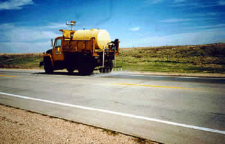 Figure 32. Photo. Topical Application of a Pavement near Wolsey, SD. This photo shows a truck spraying the solution onto the pavement.