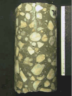 The photo shows a concrete core extracted from the deck. The core is positioned vertically and shows the profile of a crack, which is about 60 millimeters deep. Damaged coarse aggregate particles are situated in the area of the crack and below. This aggregate is quartzose gravel susceptible to A S R