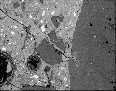 In a magnified view of a concrete lapped surface, a crack filled with reaction product extends from within a coarse aggregate particle through mortar.