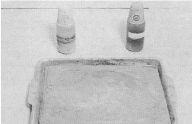 An ordinary flat pan is used to catch the grinding slurry that overflows the edge of the glass. The two plastic bottles have holes in the screw on covers and waxed paper cups for dust covers. Dry grit is shaken from the bottles and mixed on the plate with lubricant to produce a slurry.