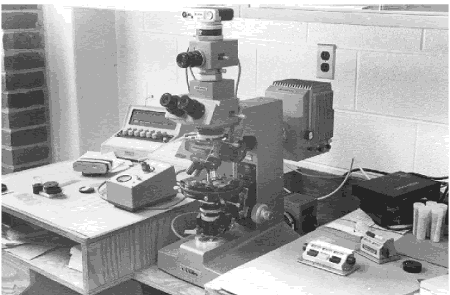 On this microscope, the stage positioning is manually operated. The nosepiece holds three objective lenses. Light can be transmitted up from the bottom through thin translucent specimens, which can be observed through the eyepieces, or a picture can be taken using the camera mount on top.