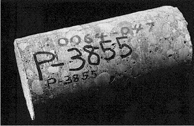 The original construction number is not obscured, and the P number is marked with a felt marker and graphite. The photo shows a cylindrical concrete core with a P-number on its surface. The number is written clearly below the original construction number in felt marker and also in graphite, and it is easily distinguished from other designations on the core.