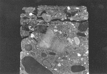 To photograph the cracking, the specimen was glued back together with a dark glue, and then cut vertically across the layered cracking. The photo shows a longitudinal cross section of a cylindrical concrete core showing sections of the aggregates and cement paste. No entrained air is apparent, and the top portion of the core shows several horizontal layers that have cracked and produced scaling and spalling